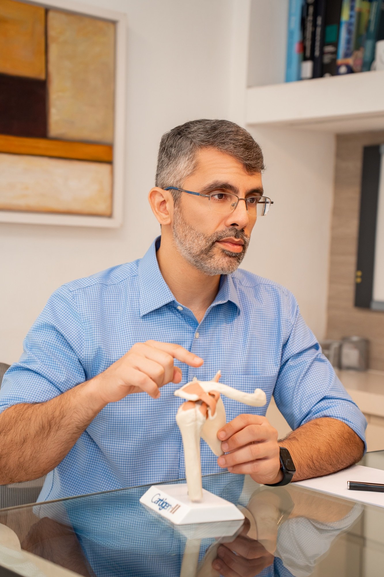 Dr. Gláucio Siqueira explicando a anatomia do ombro com modelo articulado durante consulta
